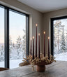 Large Baburu Bowl in Chocolate Brown by 101 Copenhagen, styled with tall black taper candles and white berry branches on a rustic wooden dining table, with snowy woodland views through the windows.