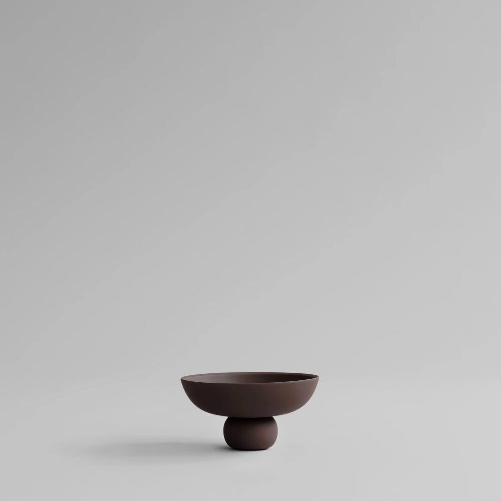 Baburu Bowl Mini by 101 Copenhagen in chocolate brown ceramic, featuring a wide, shallow bowl balanced on a small rounded base, photographed against a white background.