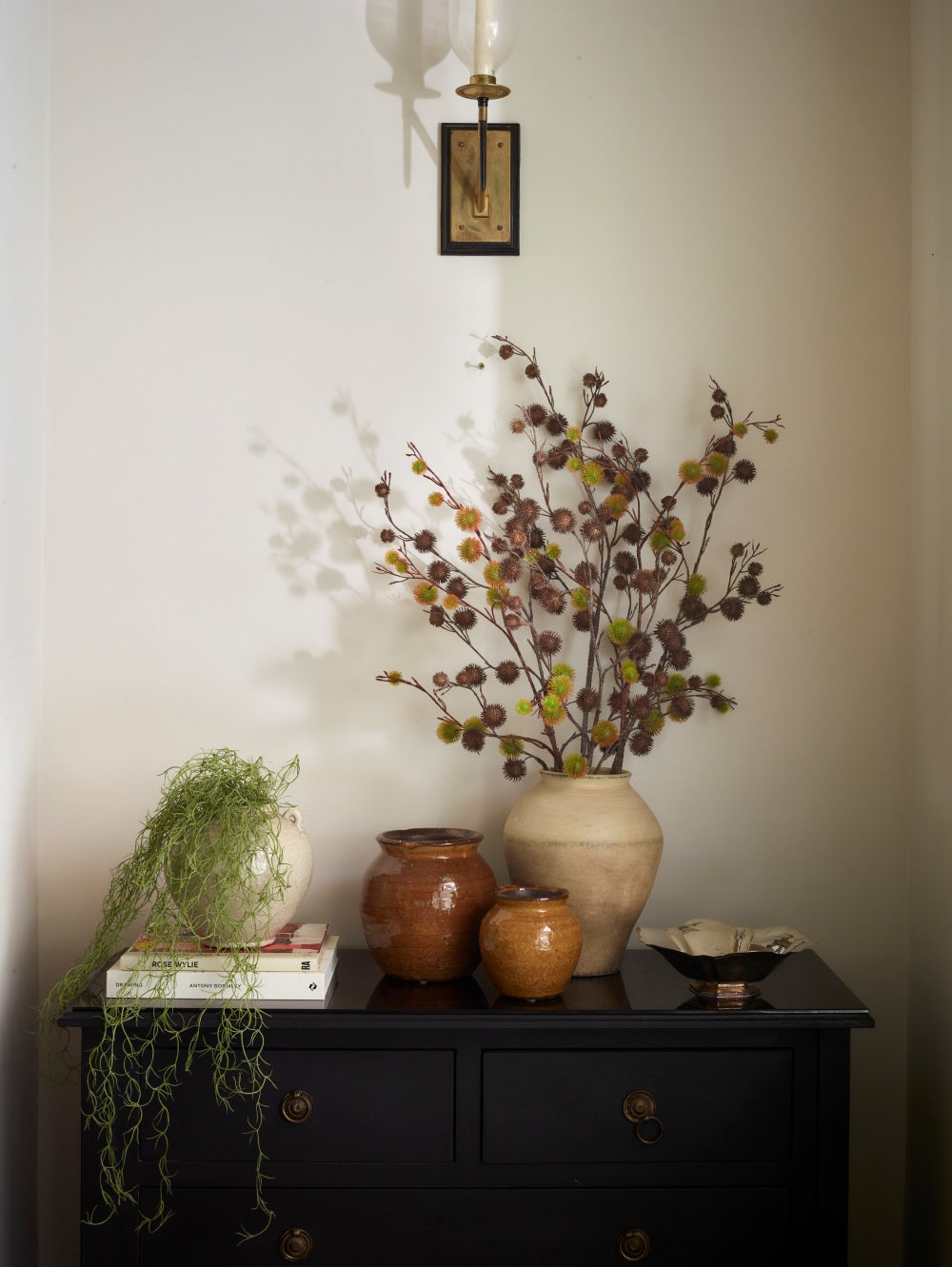 Brown Faux Chestnut branches by Fake It Flowers, featuring spiky chestnut casings arranged in a cream ceramic vase on a black cabinet in a traditional interior.