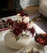 Burgundy Faux Spider Chrysanthemums by Fake It Flowers, arranged in a cream ceramic vase on a marble table with decorative accessories and grapes.