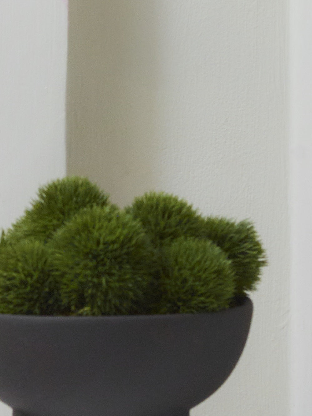 Close-up of Faux Dianthus in Green, featuring rounded clusters of fine, spiky artificial foliage arranged in a dark decorative bowl against a neutral background.