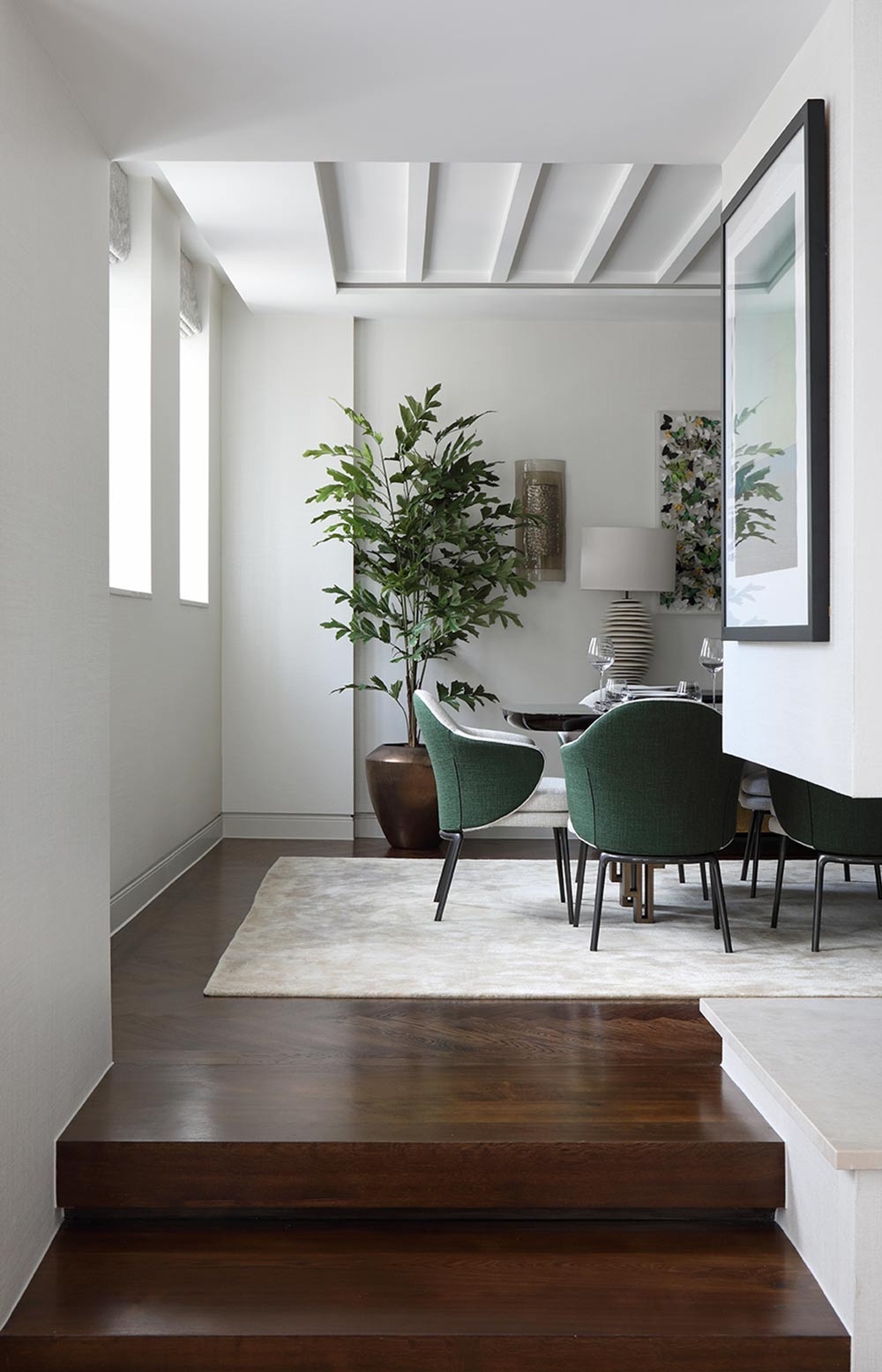 Modern interior with a staircase leading to a dining area with green chairs and a plant.
