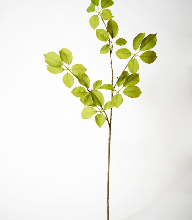 A single decorative faux fruit leaf branch with bright green leaves and a brown stem, photographed against a clean white studio background.
