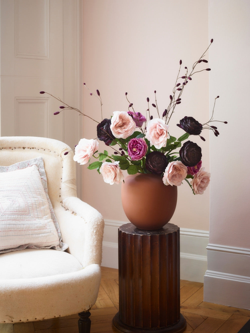 A beautiful array of faux flowers in a brown vase on a wooden plinth including a chiffon pink rose.