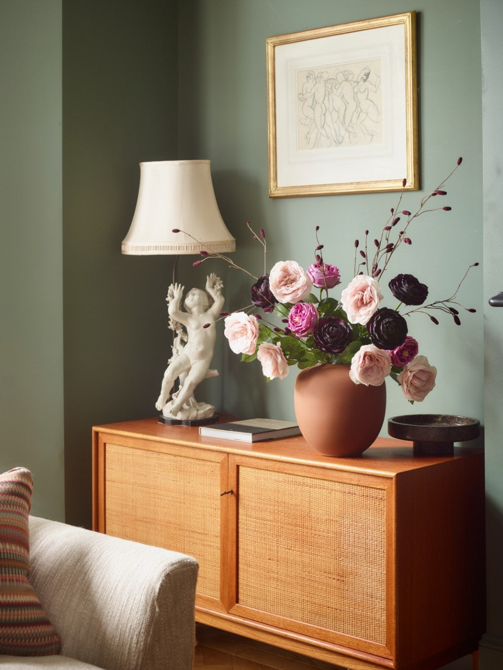 bouquet of faux flowers including chiffon pink roses in a brown vase on a sideboard in a sage green living room  