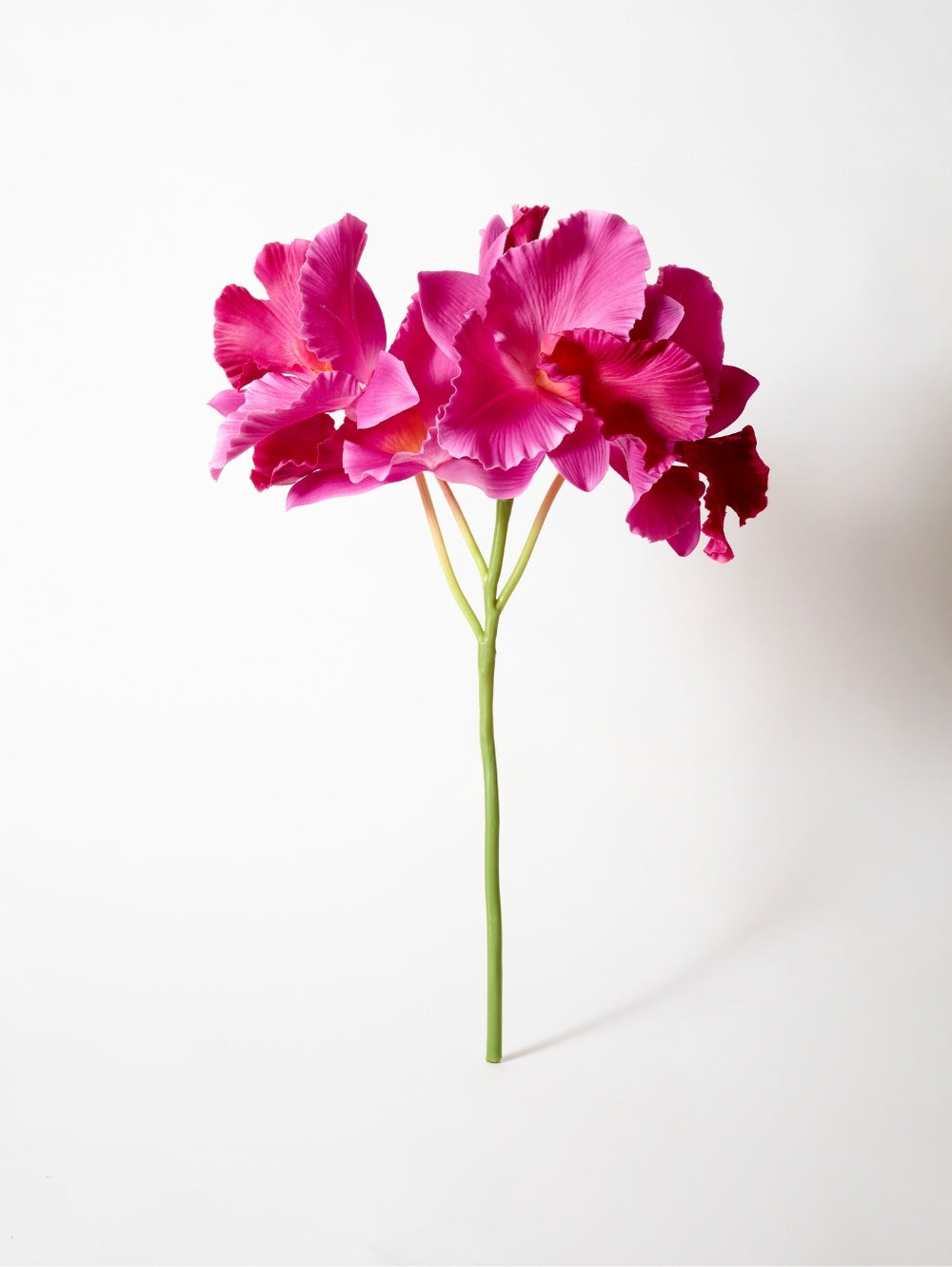A single stem of artificial vibrant magenta-pink Vanda Orchid flowers with ruffled petals and a green stem, photographed against a clean white background.