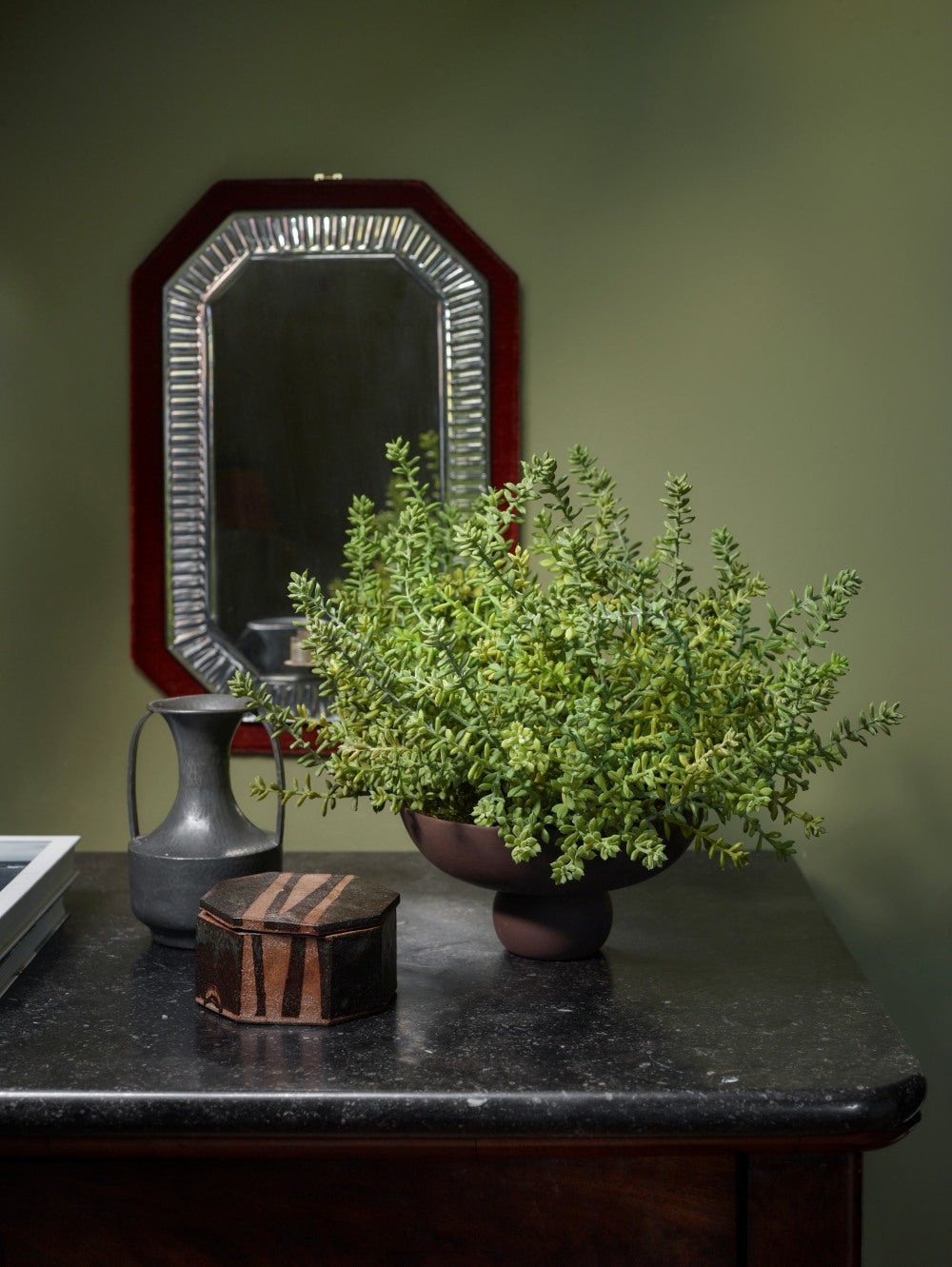 Brown Baburu Bowl Mini by 101 Copenhagen, styled with a generous arrangement of green foliage on a dark marble console table, alongside decorative objects and a framed mirror.