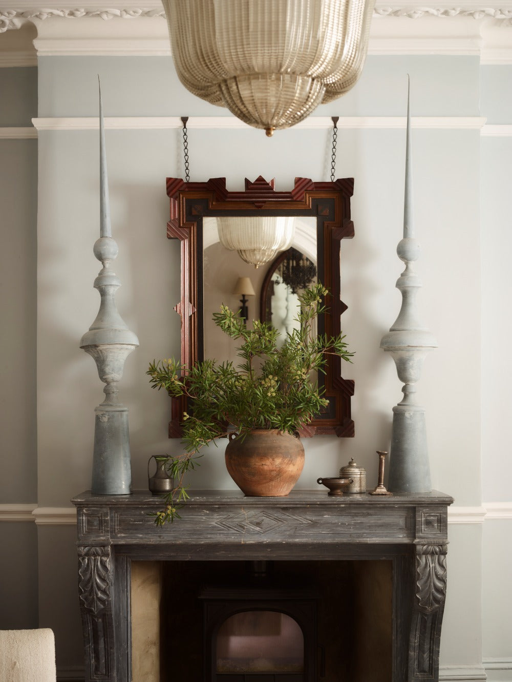 Faux Podocarpus Green by Fake It Flowers, arranged in a rustic ceramic vase on a marble fireplace mantel beneath an antique wooden mirror.