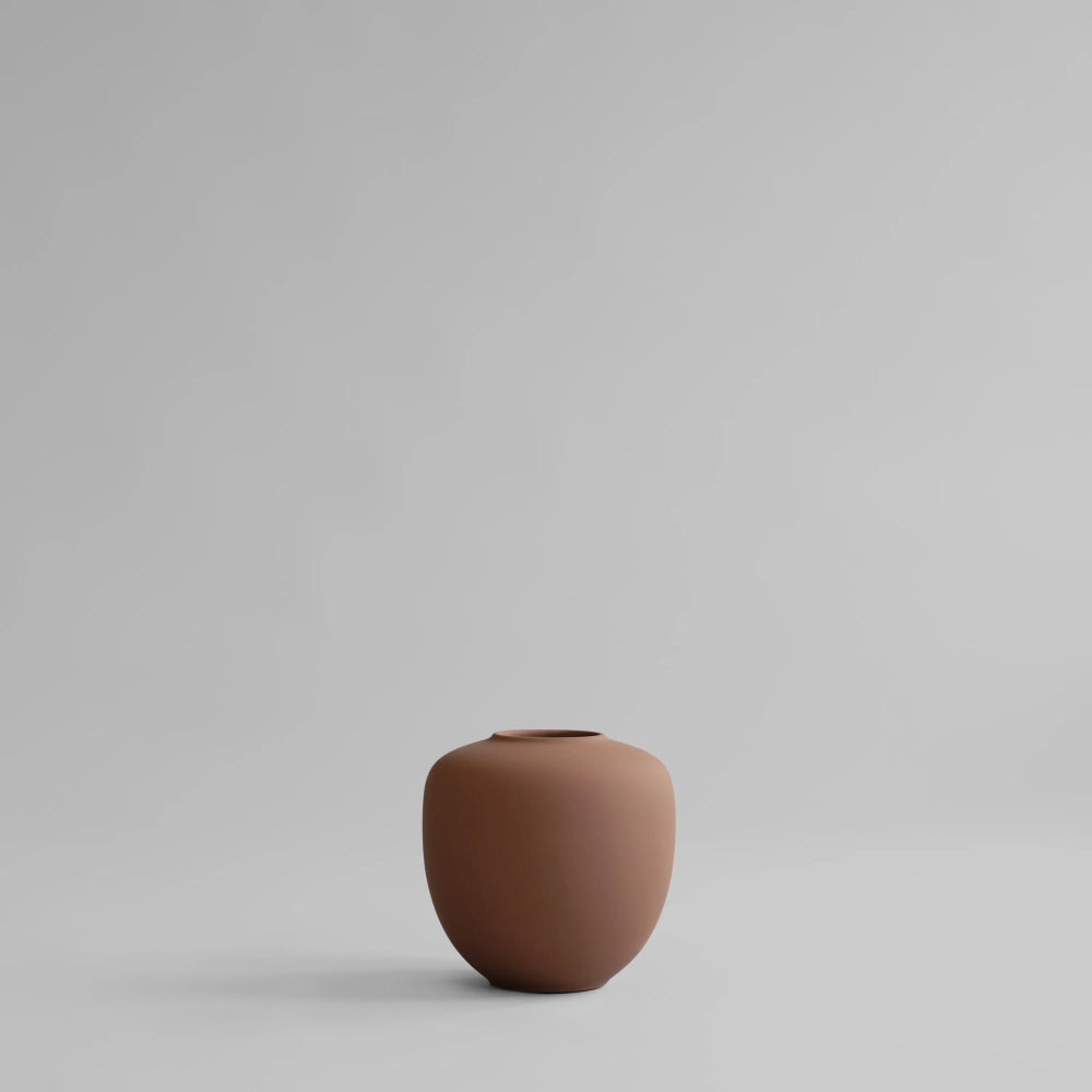 Sunao Vase Mini by 101 Copenhagen in Almond, featuring a rounded sculptural silhouette, narrow opening and smooth warm brown finish, photographed against a neutral background.