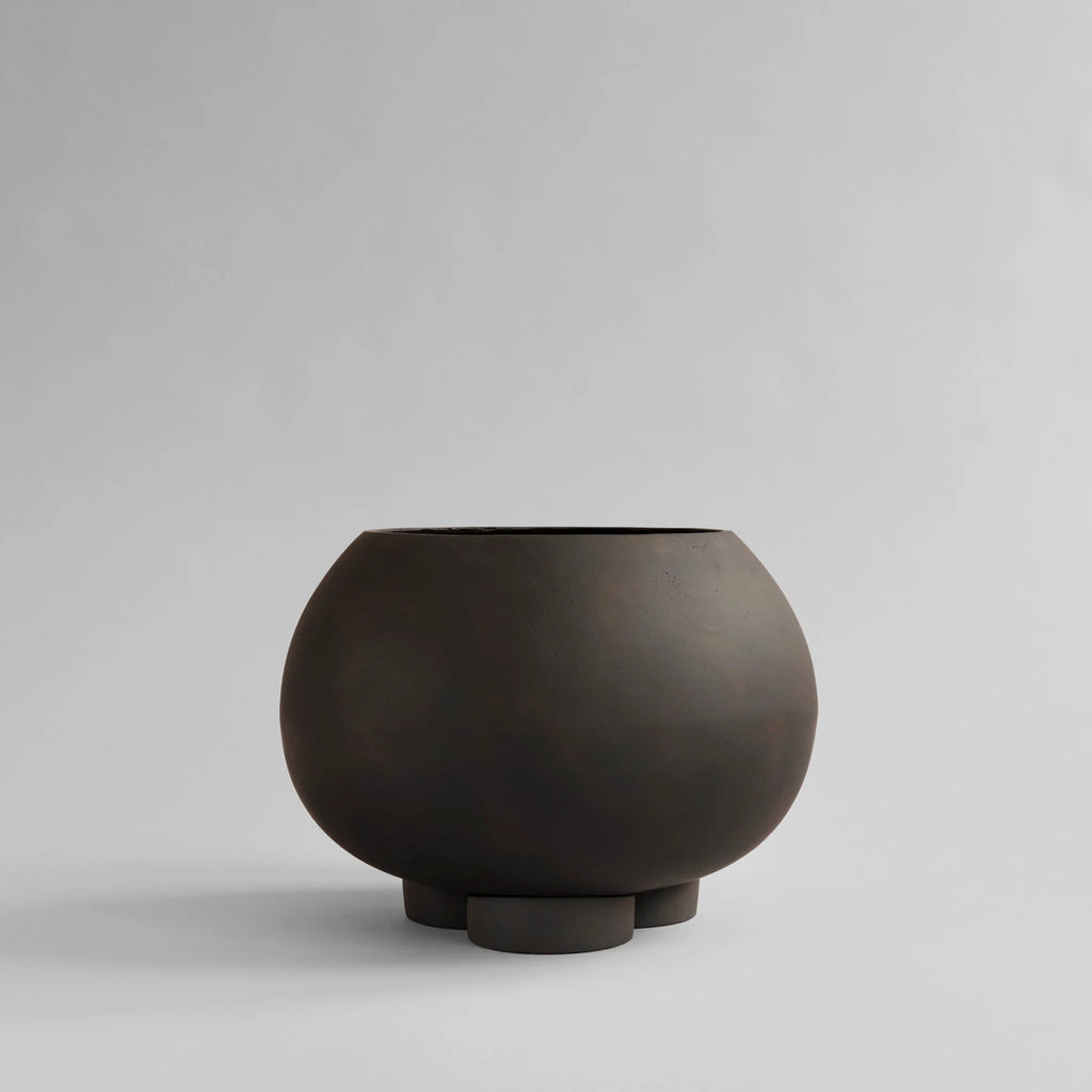 Urchin Plant Pot Medio in Coffee by 101 Copenhagen, featuring a wide, rounded ceramic vessel with a matte dark brown finish, open top and three sculptural legs, photographed against a light background.